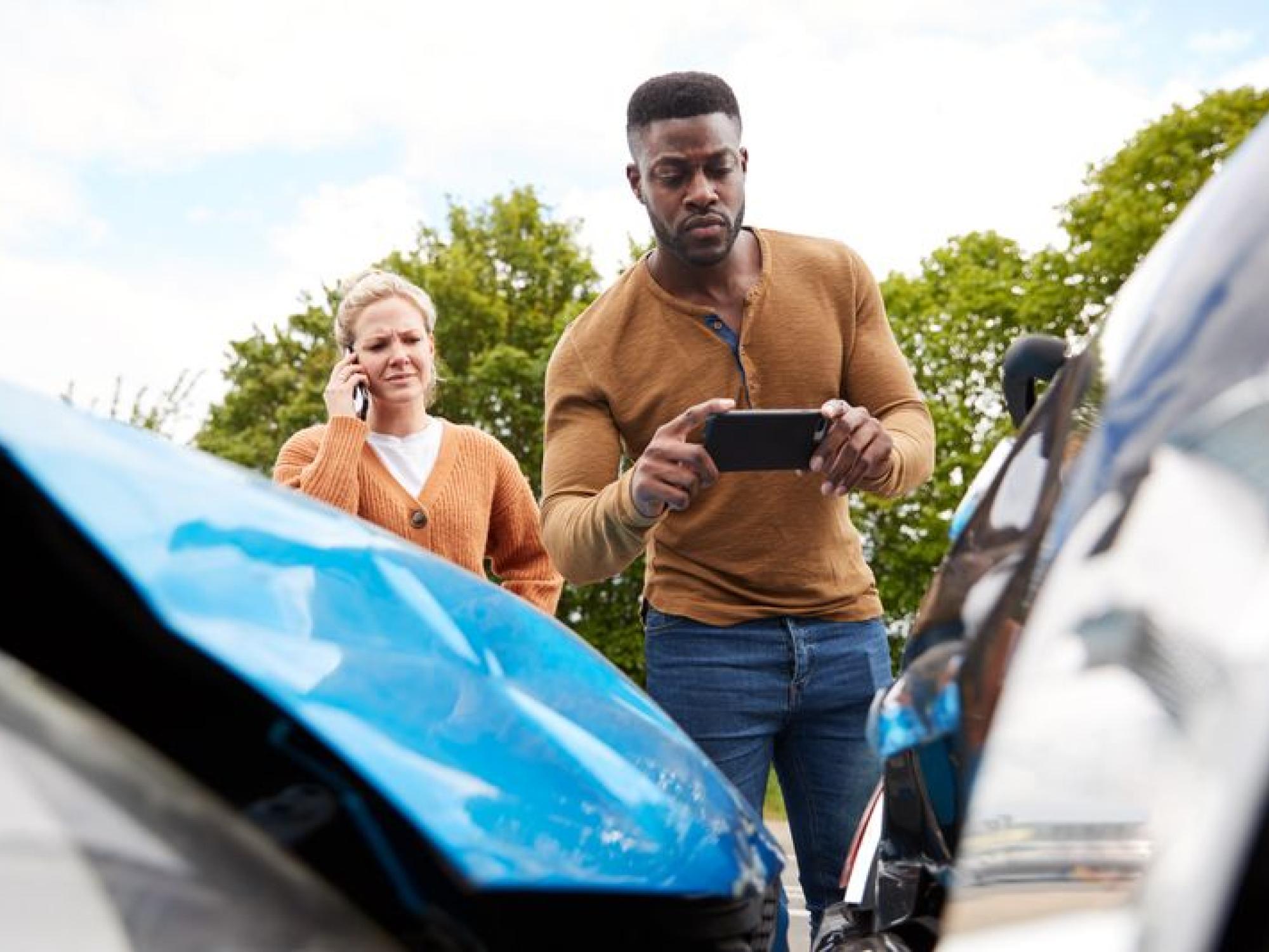 black man holding a phone in front of two collided cars